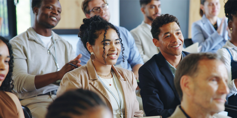 An audience of job seekers are listening intently, looking towards the speaker and smiling.