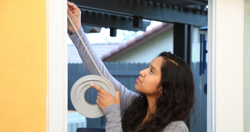 Woman adding weatherstripping to her doorway to save energy costs