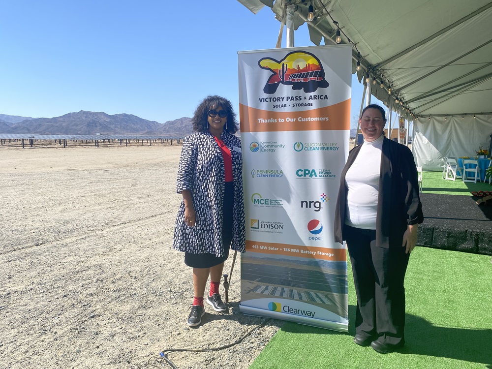 Two women pose in front of a Clearway Energy banner with a solar array in the background. 
