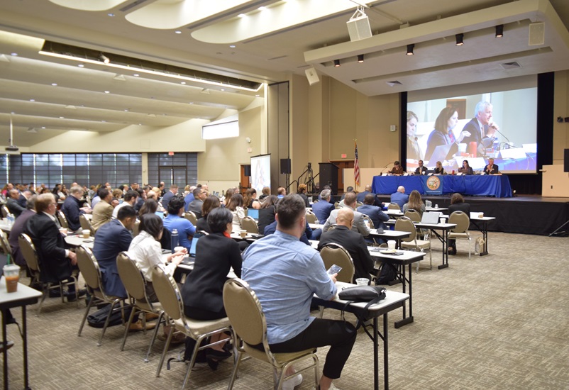 Five Public Utilities Commissioners preside over a large conference room of attendees. 