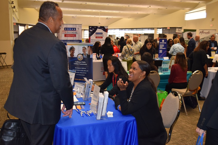 Two expo attendees have a lively conversation over a table with a blue tablecloth 