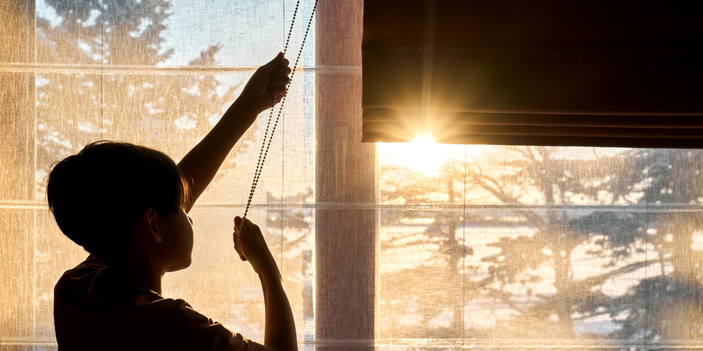 Young person lowering blinds against a sunny sky